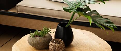 A wooden table with two vases and a plant, a black chair, and a beige sofa with patterned cushions.
