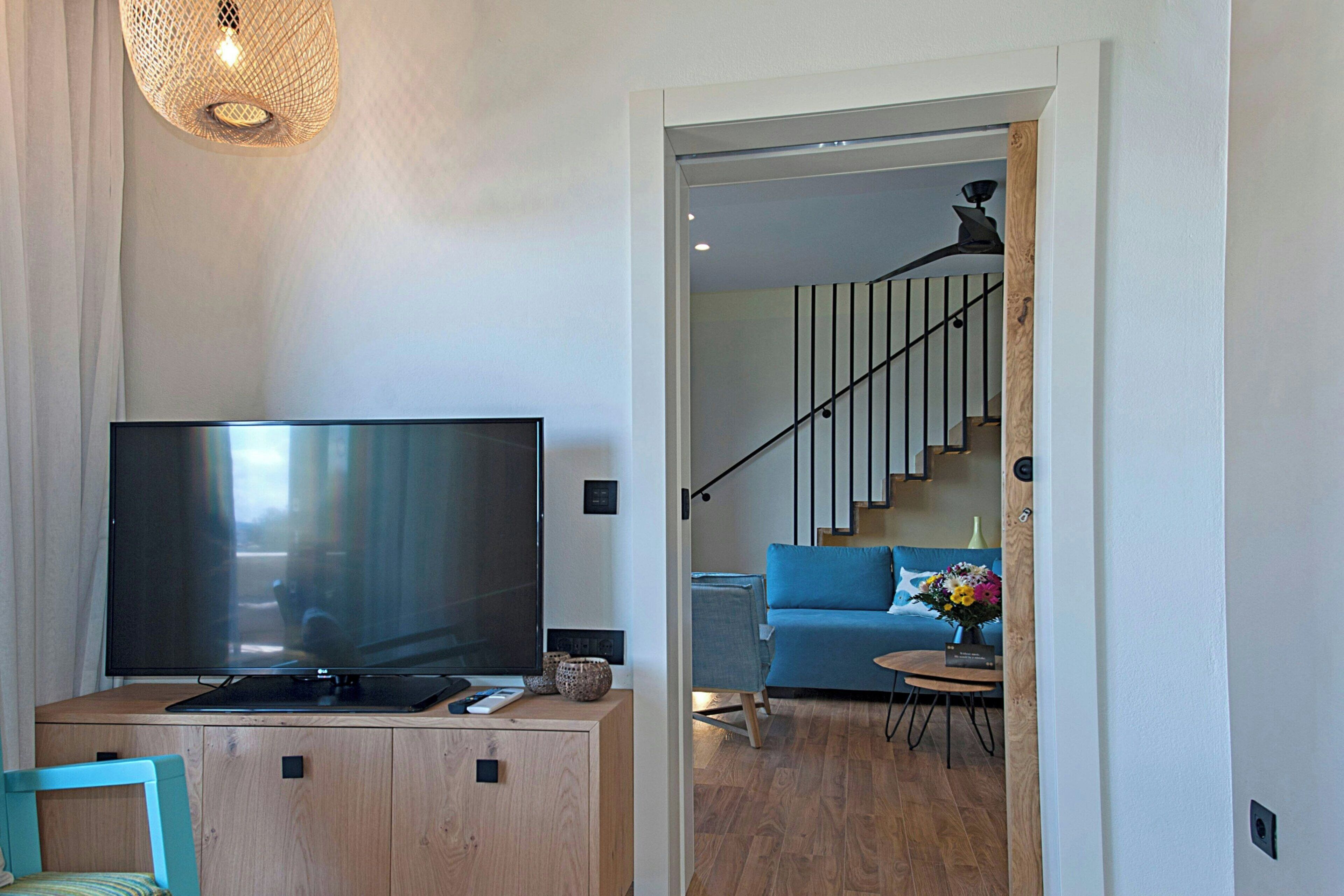 A modern living room with a flat-screen TV on a wooden cabinet, a blue sofa, and a staircase leading to an upper floor.