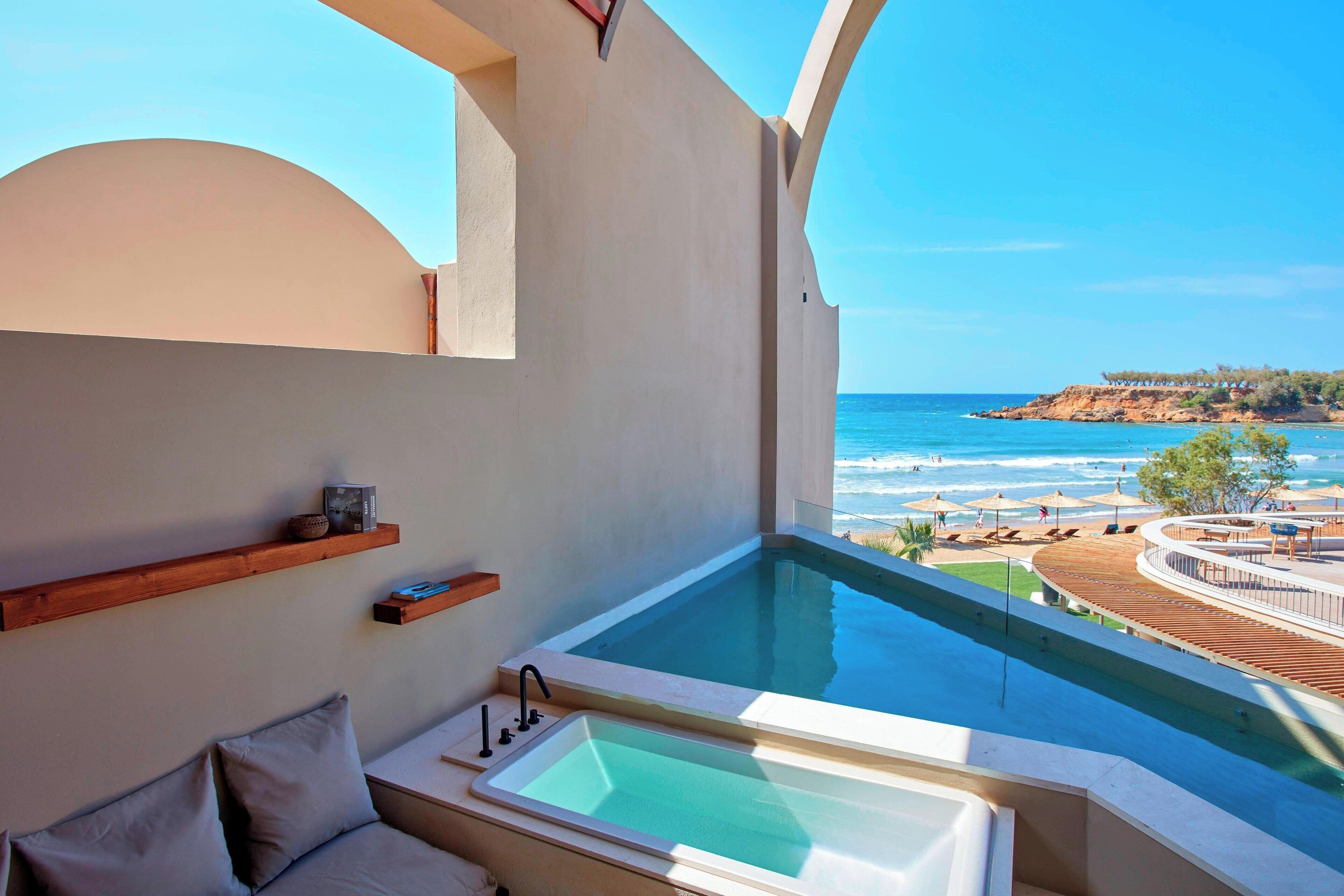 A balcony with a view of the ocean, a bathtub, and a sofa.