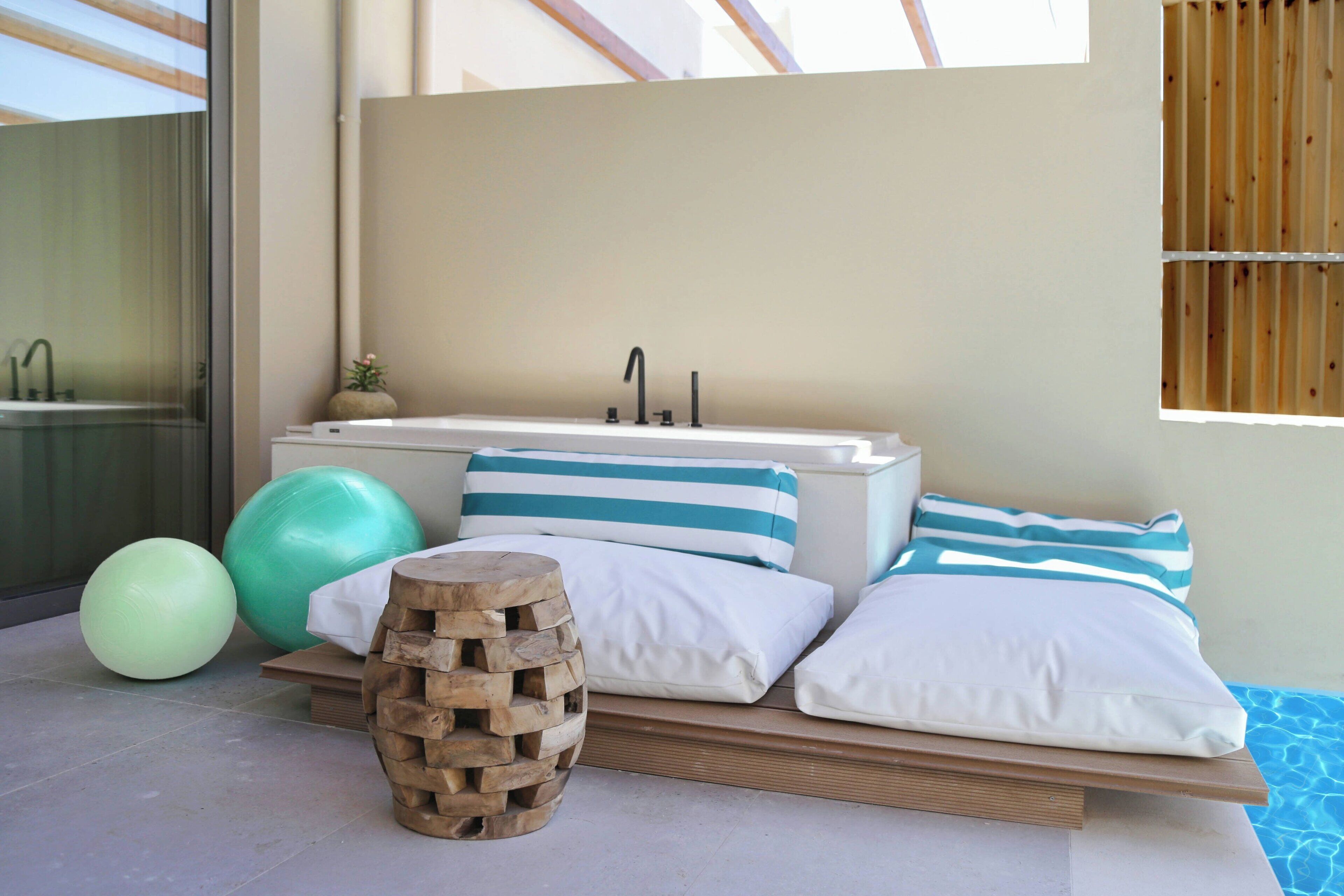 Un baño moderno con una bañera, un taburete de madera y pelotas de ejercicio.
