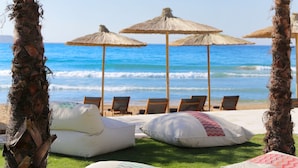 Un área de descanso frente a la playa, con palmeras, sombrillas de paja y sillones.