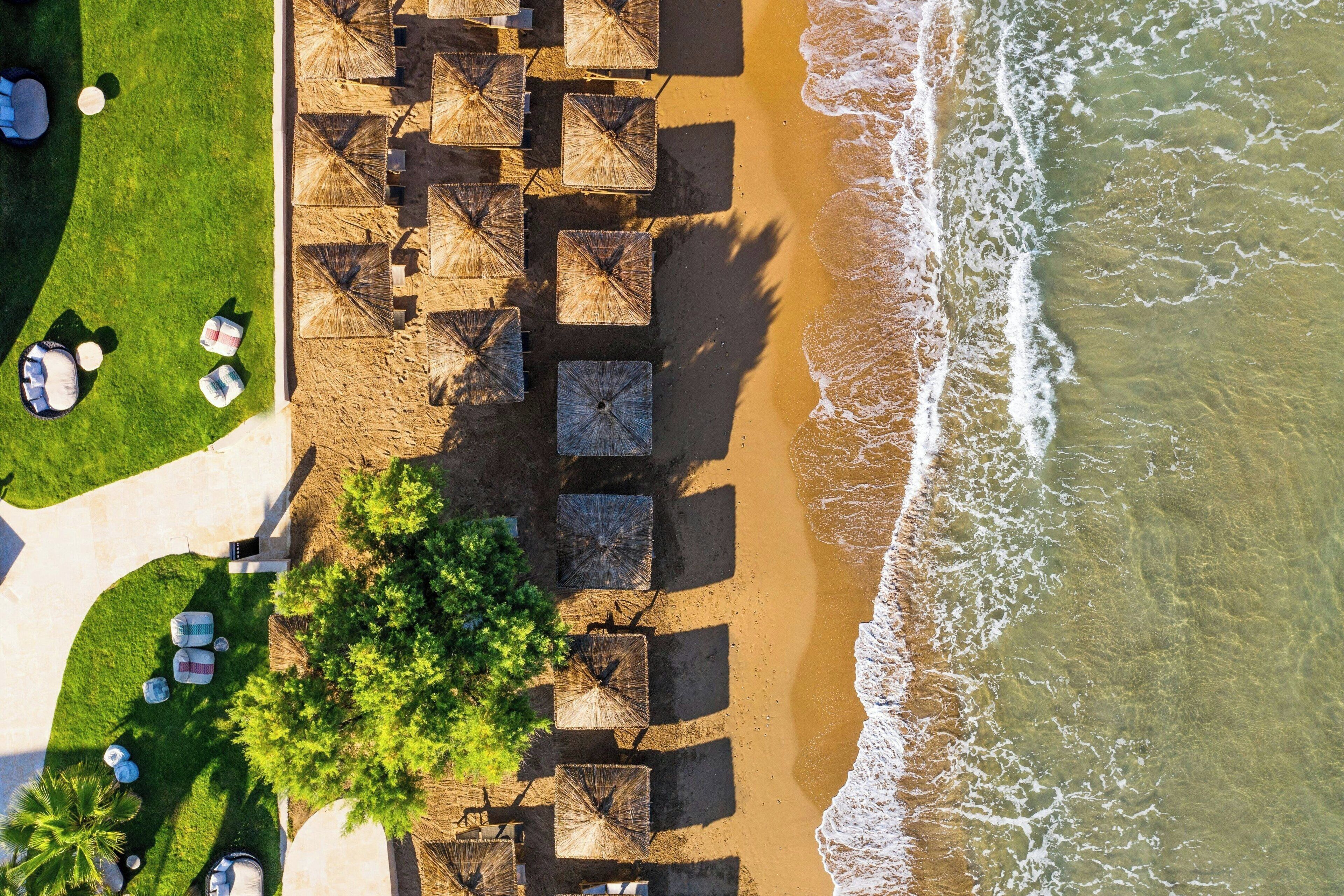 Luchtbeeld van een strandresort met parasols, ligstoelen en een pad dat naar het strand leidt.