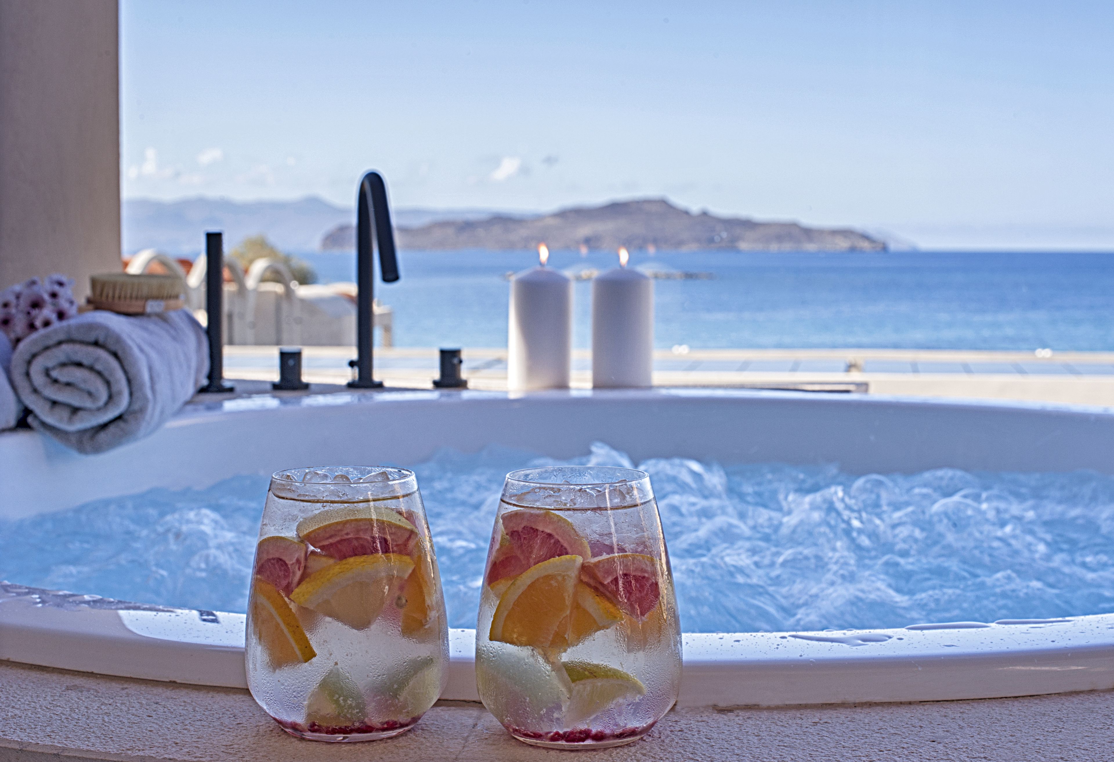 Two glasses of iced beverage with fruit slices on a balcony with a hot tub and a view of the sea.
