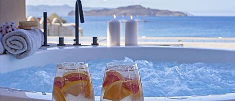 Two glasses of iced beverage with fruit slices on a balcony with a hot tub and a view of the sea.