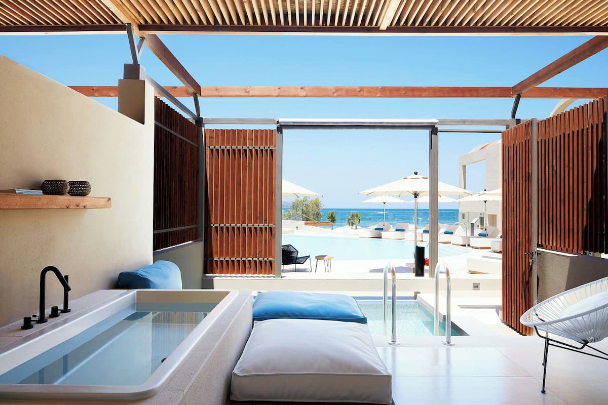 Ein modernes Badezimmer mit Badewanne, Dusche und Blick auf einen Poolbereich mit Sonnenschirmen.