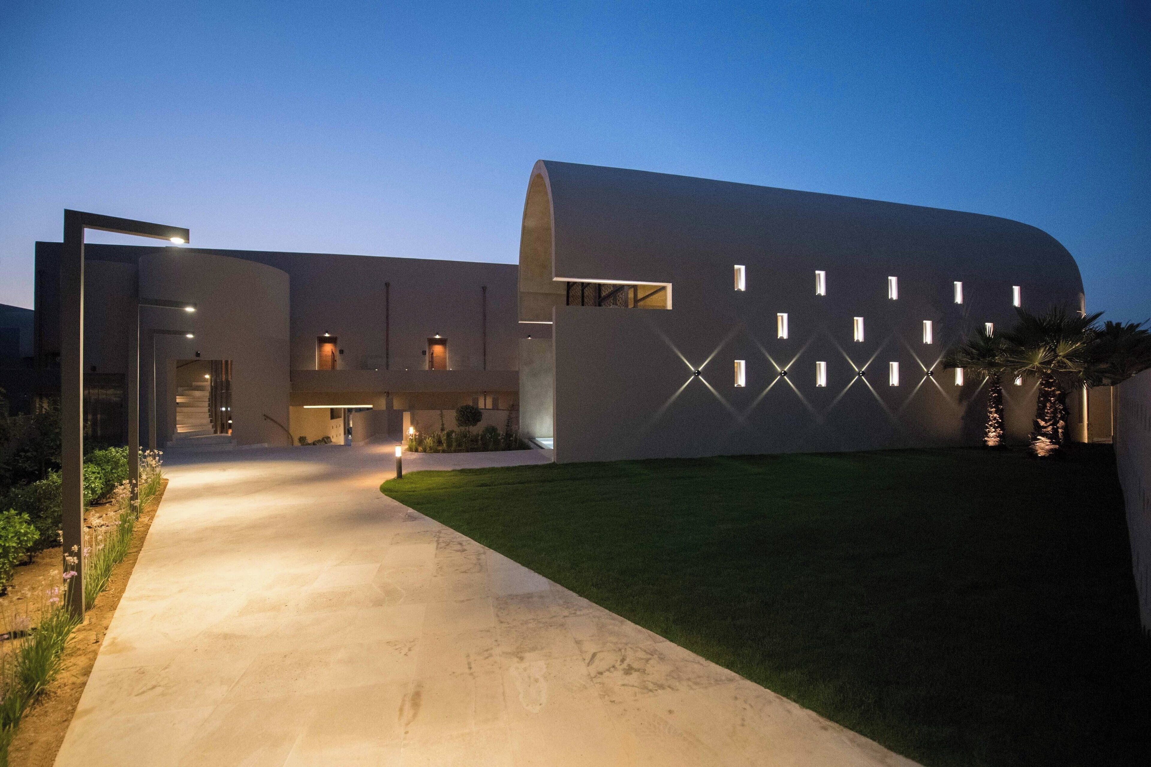 Un bâtiment moderne doté d’une façade incurvée, d’une entrée centrale et d’un chemin bien éclairé menant à l’entrée.