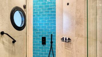 A glass-enclosed shower with a blue-tiled wall, a circular mirror, and a handheld showerhead.