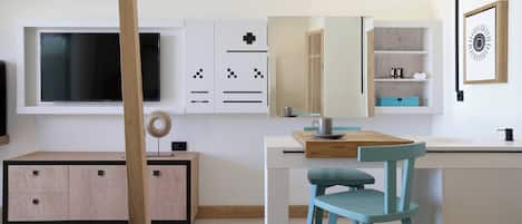 A modern kitchen with a built-in TV, wooden cabinets, a blue chair, and a dining table.