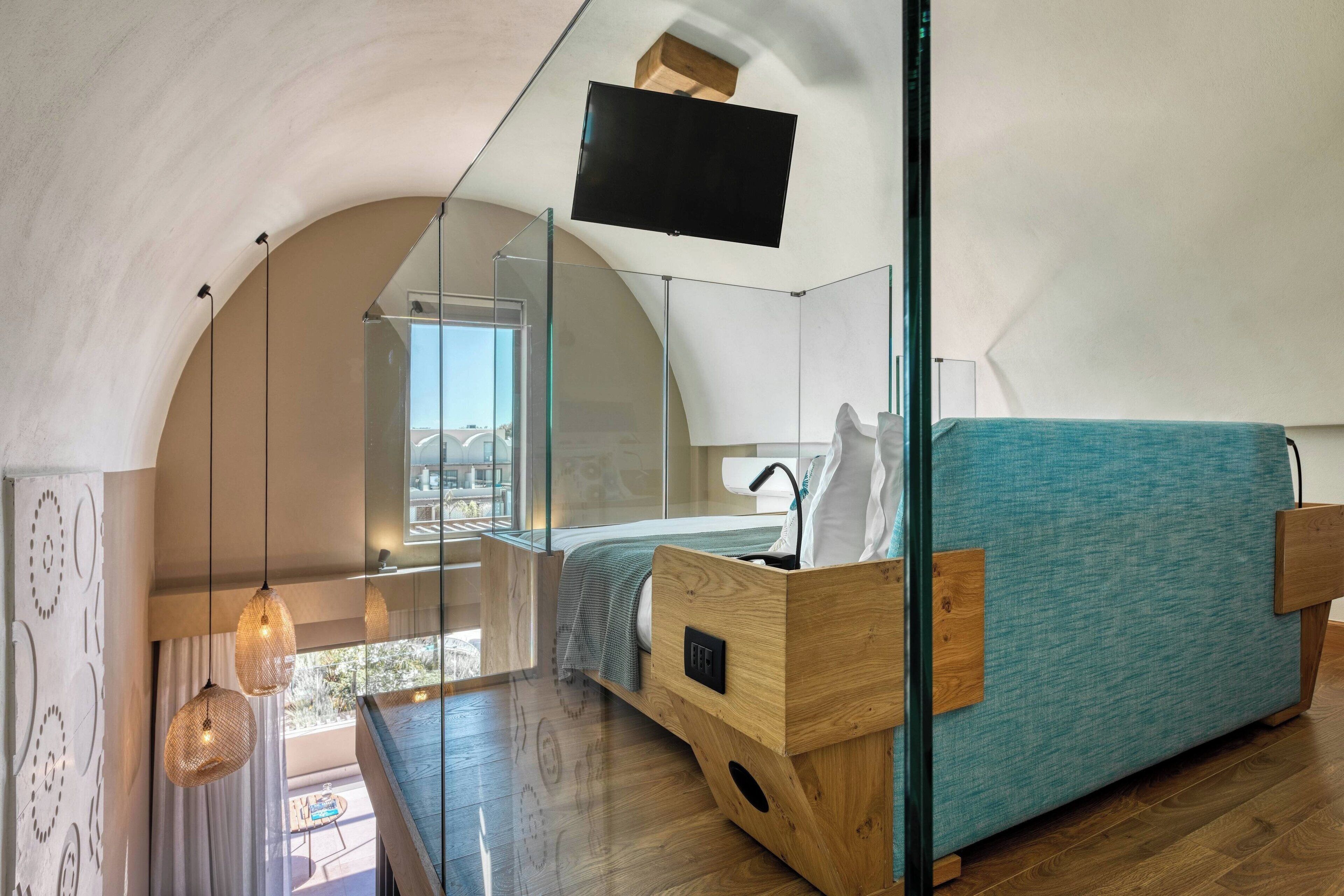 A modern bedroom with a glass partition, wooden furniture, and a mounted TV.