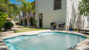 A swimming pool with a tiled deck, surrounded by potted plants and outdoor furniture. - Peo Luxury Apartments (Maun)