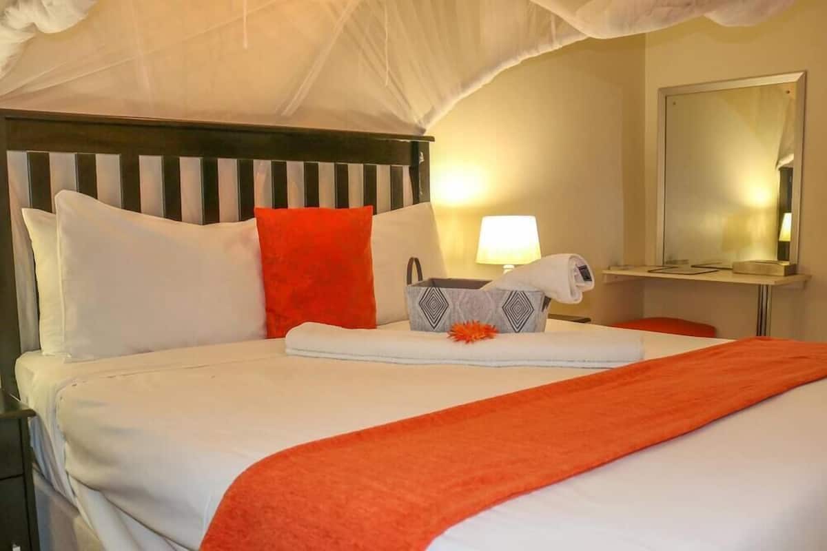 A hotel room with a bed, a bedside table, a lamp, and a mirror.