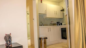 A compact kitchen with white cabinets, a tiled backsplash, and a small countertop. - Peo Luxury Apartments (Maun)