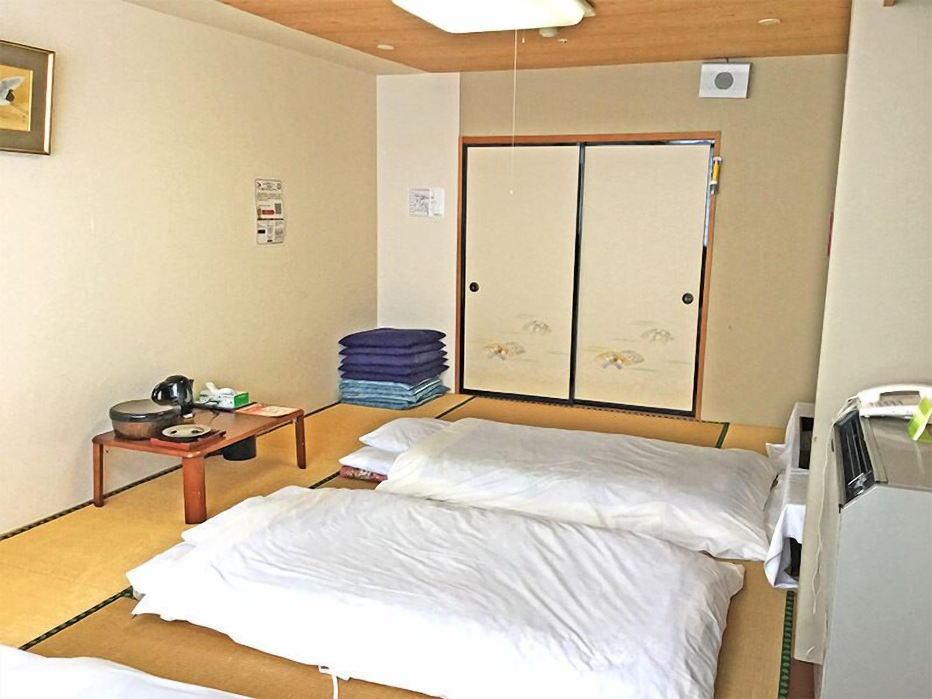 Hotelkamer met een bed, een klein tafeltje met waterkoker, een stapel opgevouwen kleding en een kledingkast met schuifdeur.