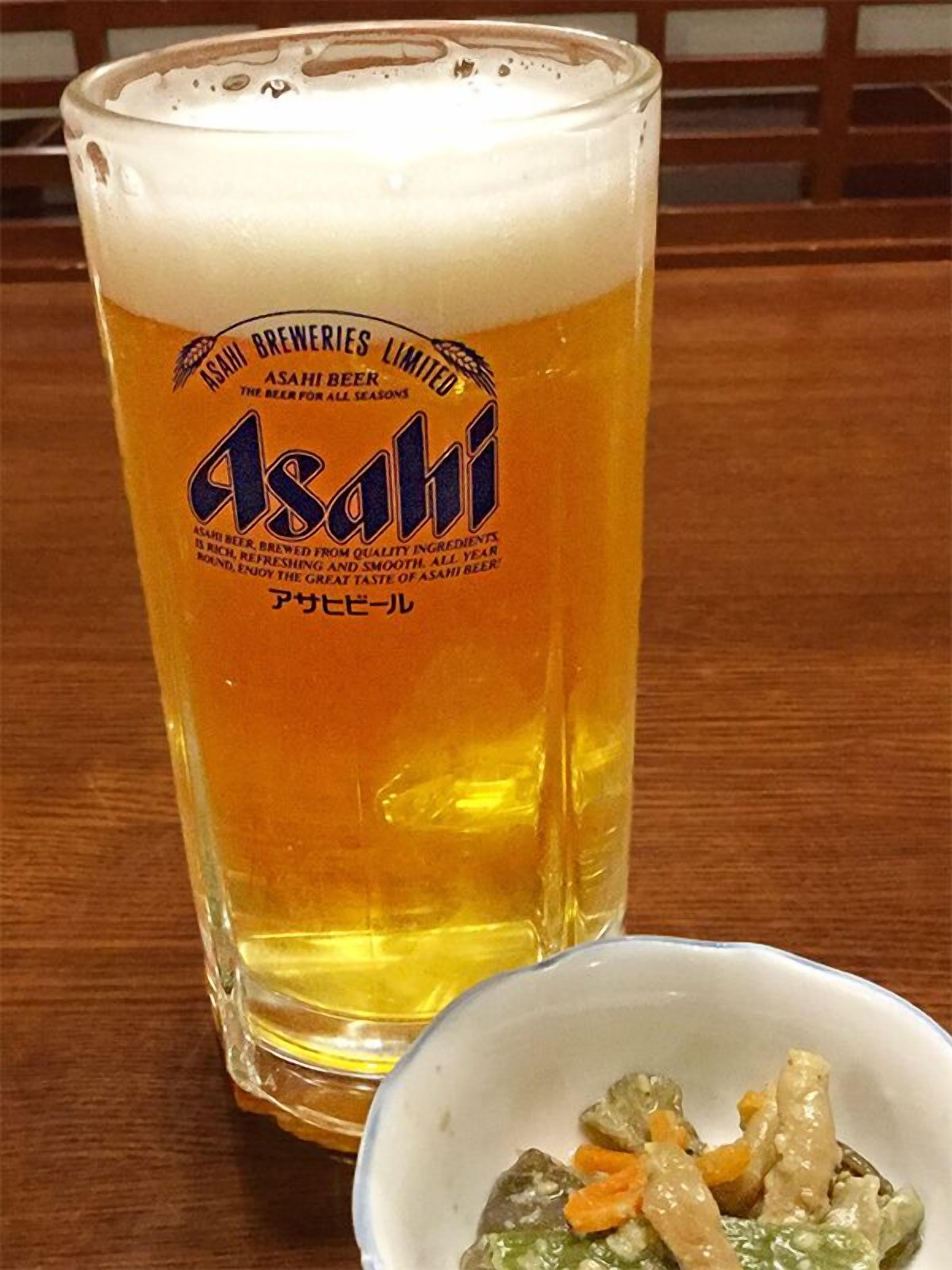 A glass of Asahi beer with a label, and a small bowl of food beside it.