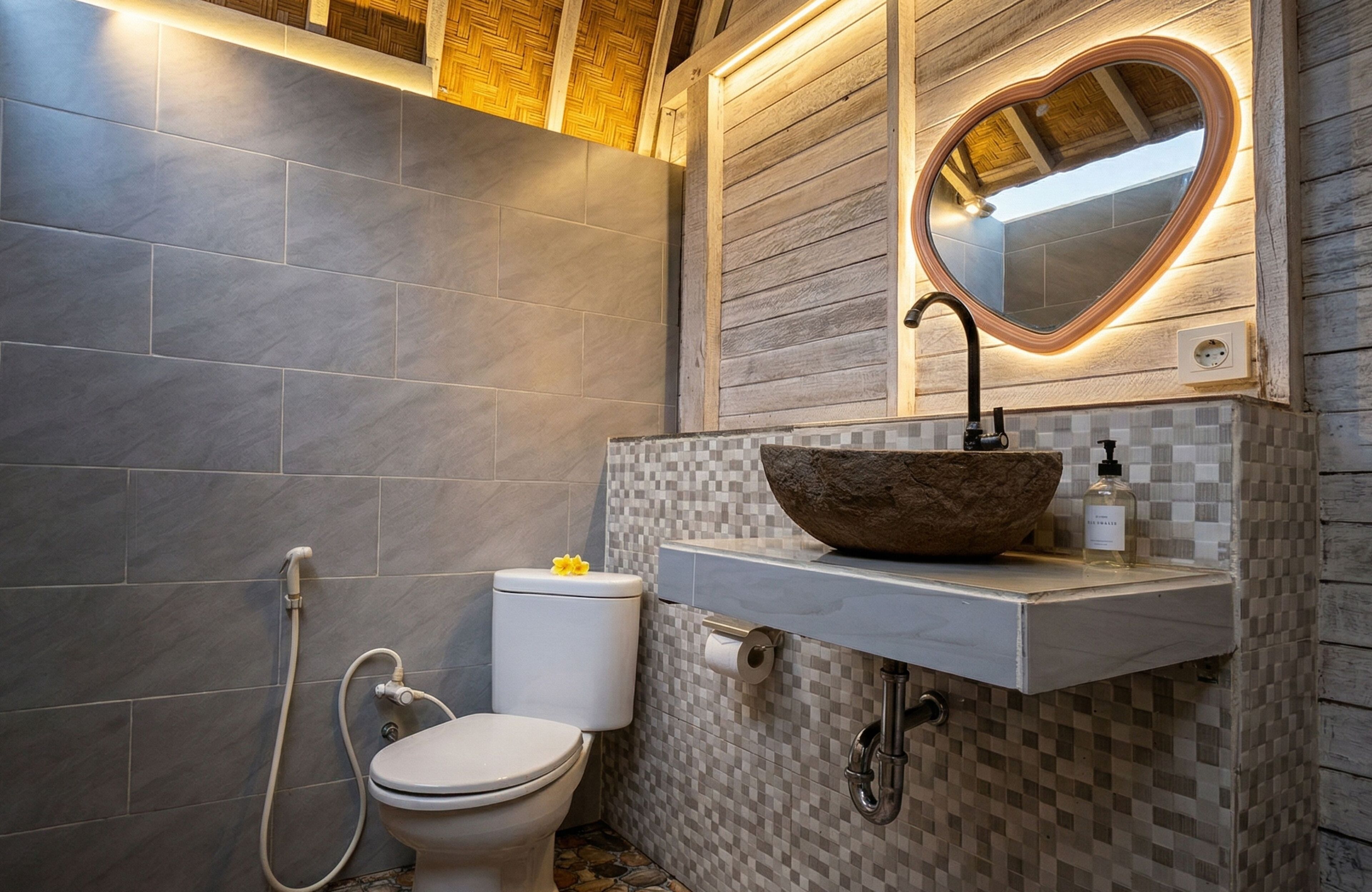 Une salle de bain avec des toilettes blanches, un miroir en forme de cœur et un lavabo sur colonne.