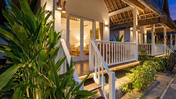 Een vakantiehuis aan het strand met een overdekte veranda, buitenmeubels en een goed verlichte ingang.
