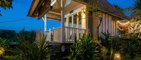 A house with a porch, surrounded by tropical plants and a small water feature.