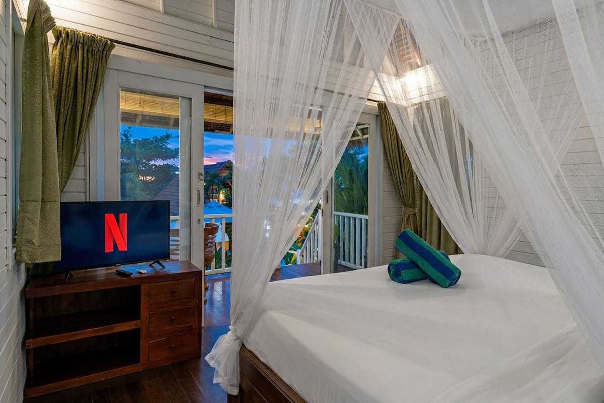 Een slaapkamer met een televisie, een bed met hemelbed en een balkon met uitzicht.