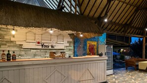 Een bar met rieten dak, een toog met het bord 'Yogi BA' en een kleurrijke muurschildering op de achtergrond.