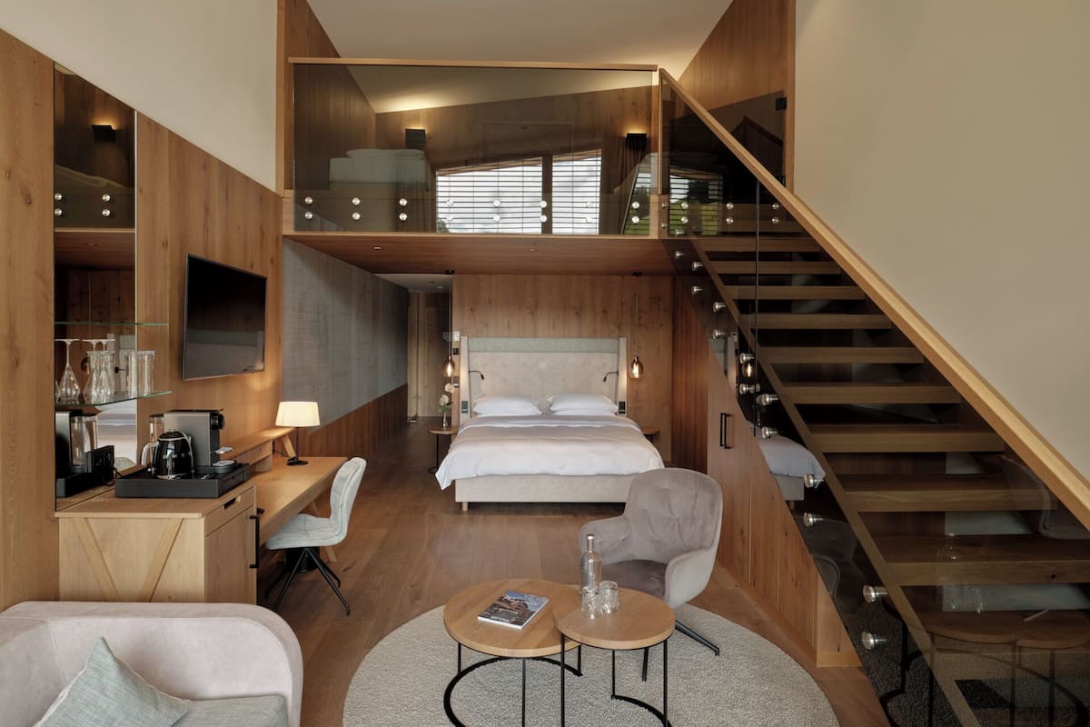 Ein modernes Hotelzimmer mit Erkerbett, einem Schreibtisch mit Computer, einem Sessel, einem runden Couchtisch und einer Treppe.