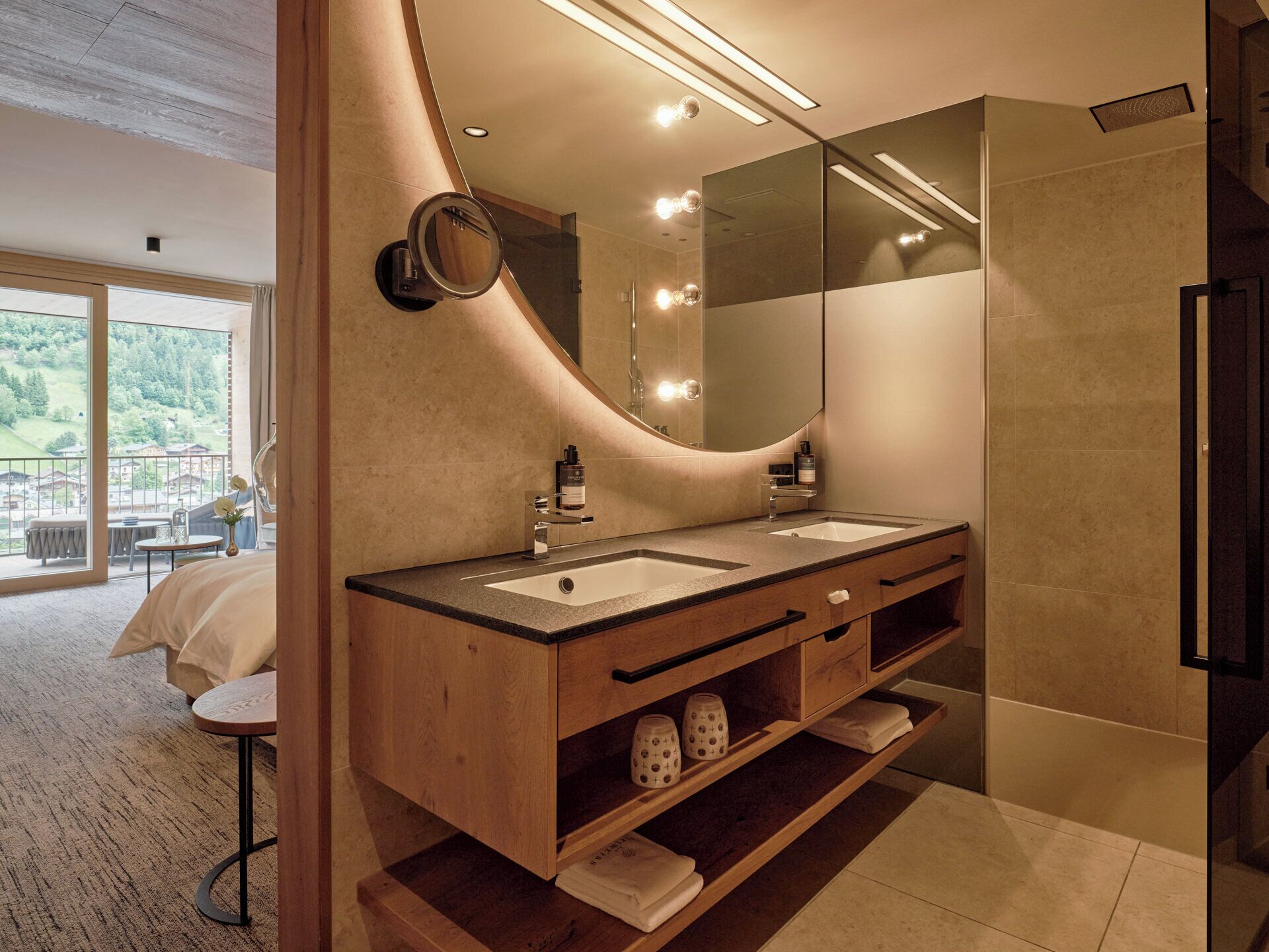 Een moderne badkamer met twee wastafels, een grote spiegel en uitzicht op een balkon met buitenmeubilair.