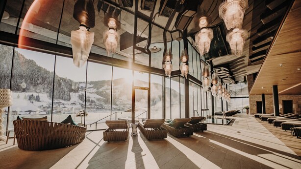 Amplio espacio interior con grandes ventanales que dan a un paisaje nevado, con mobiliario de mimbre moderno y lámparas colgantes.