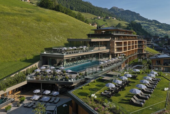 A modern hotel with a rooftop pool, multiple lounge areas with umbrellas, and a scenic hillside view. - DAS EDELWEISS - Salzburg Mountain Resort (Grossarl)