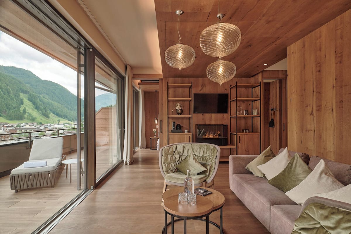 Ein großzügiges Wohnzimmer mit großem Fenster und Blick auf eine gebirgige Landschaft, inklusive Kamin und Holzvertäfelung.