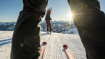 A ski slope with a person skiing and another standing in the background.