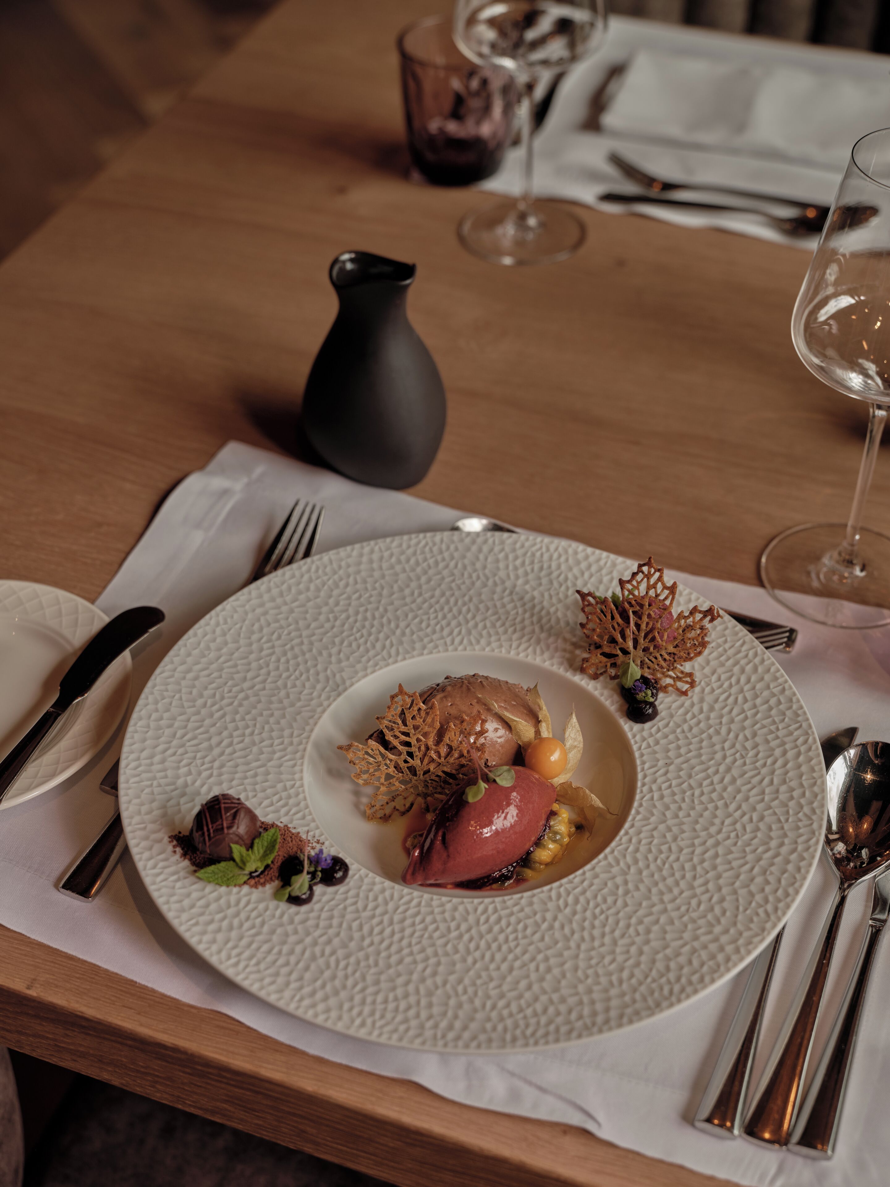 A dining table with a white textured plate, silverware, and a glass of wine.