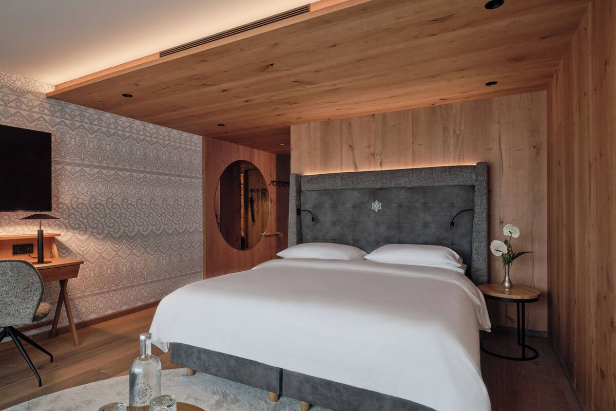Ein modernes Schlafzimmer mit einem großen Bett, einem runden Spiegel, einem Schreibtisch und einem kleinen Tisch mit einer Vase.