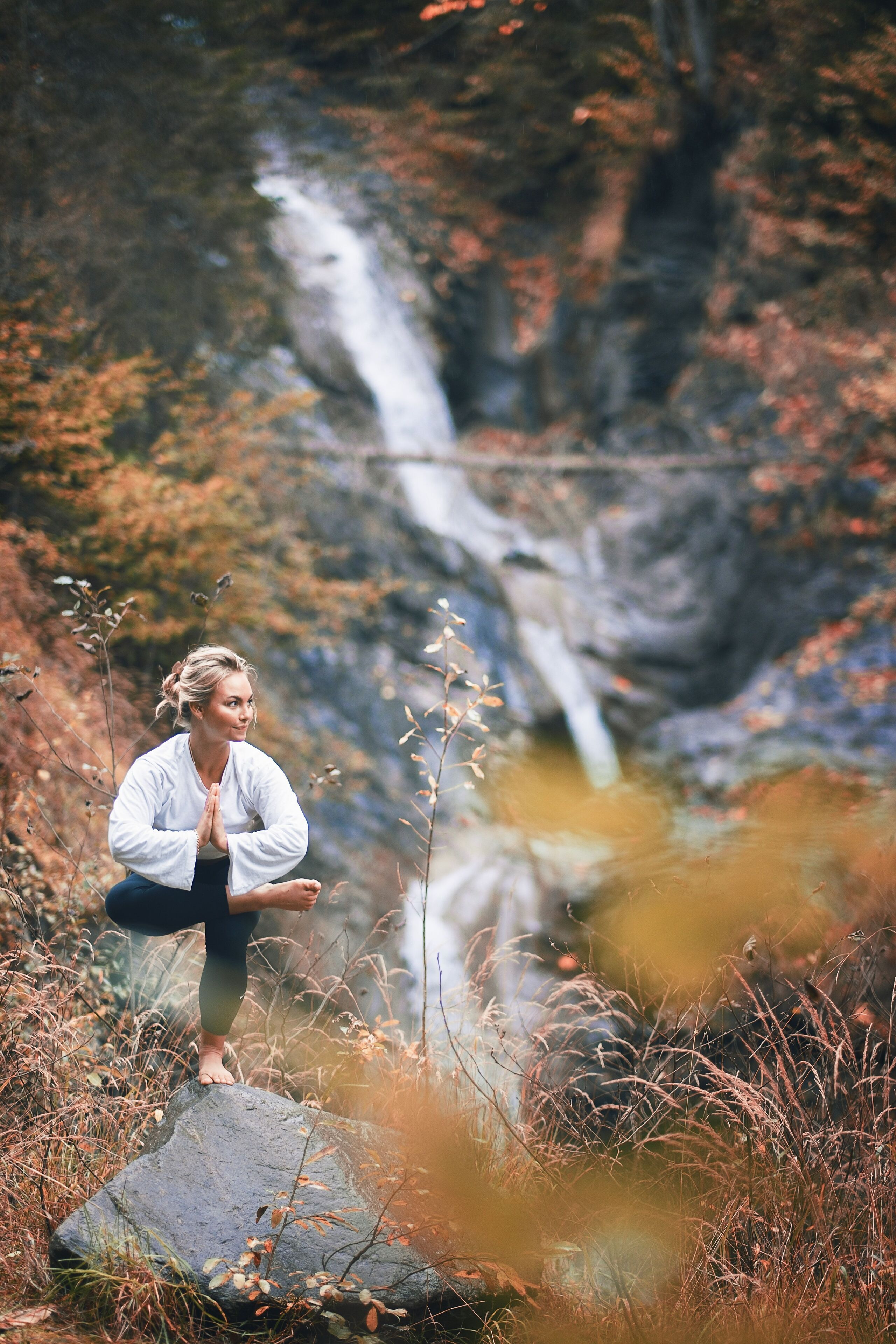 Una persona sentada sobre una roca en un entorno natural, con una cascada al fondo.