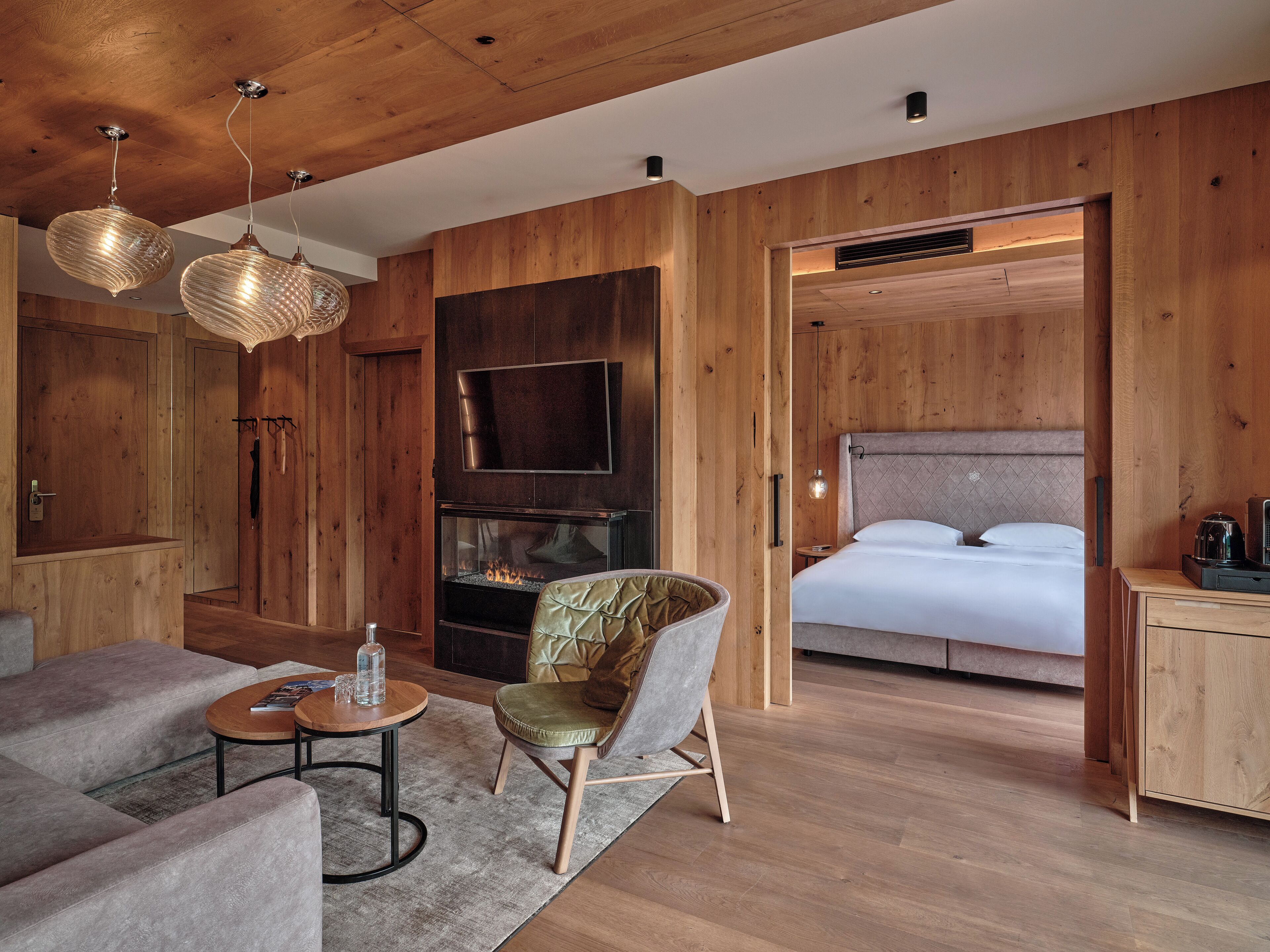 Una habitación moderna con techo de madera, chimenea, cama, televisor y zona de estar con mesa de centro y sillones.