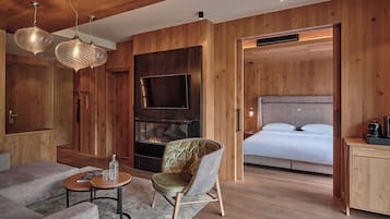 Una habitación moderna con techo de madera, chimenea, cama, televisor y zona de estar con mesa de centro y sillones.