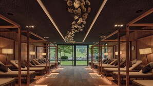 Une salle de spa moderne avec un plancher en bois, plusieurs tables de massage et une grande fenêtre donnant sur l’extérieur.