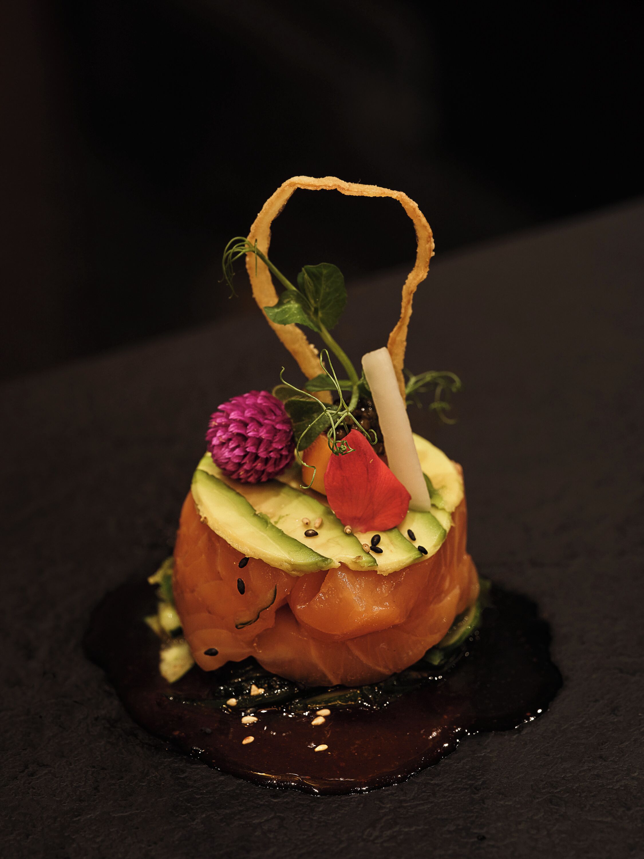 Plato con salmón, aguacate y guarniciones sobre un fondo oscuro.
