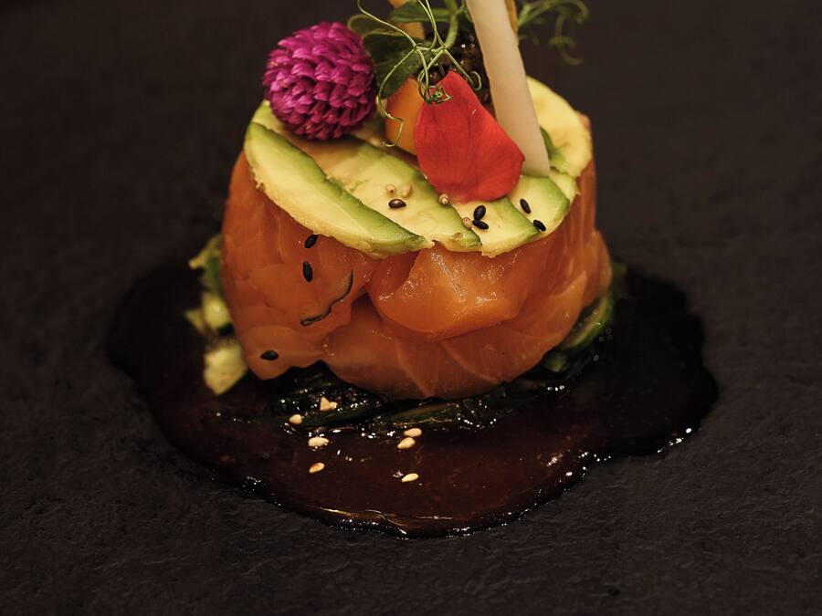 Plato con salmón, aguacate y guarniciones sobre un fondo oscuro.