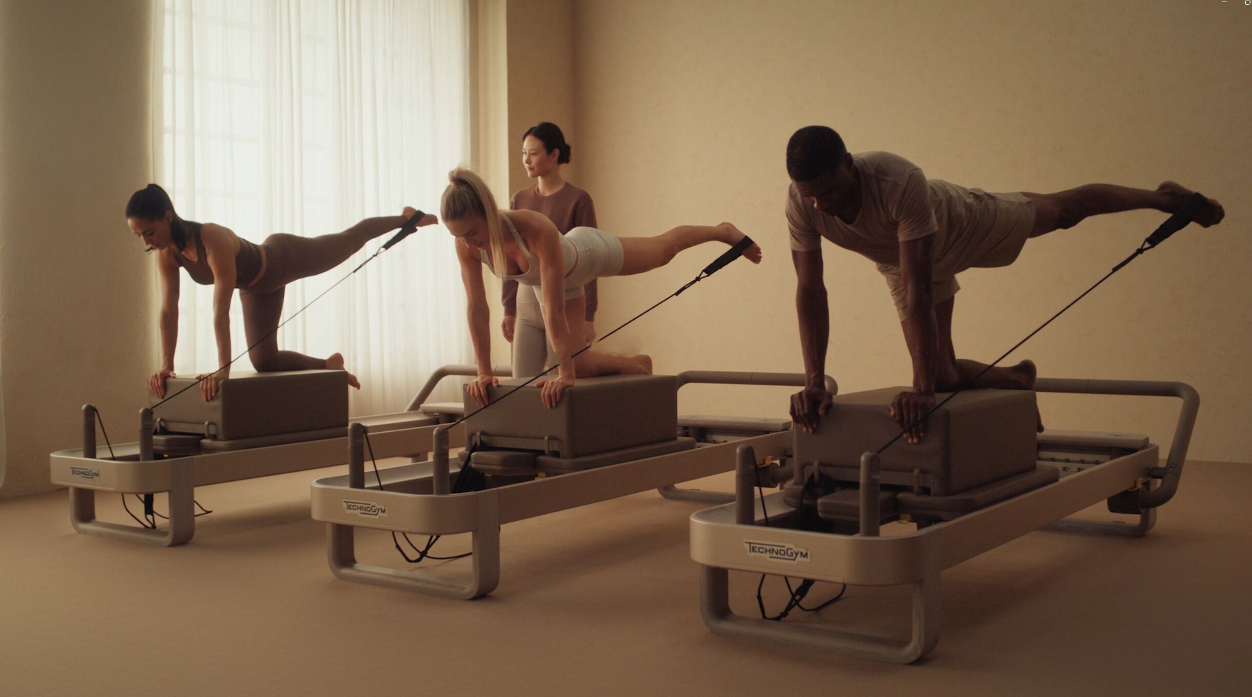Un estudio de Pilates con tres máquinas de ejercicio y una persona realizando ejercicios.