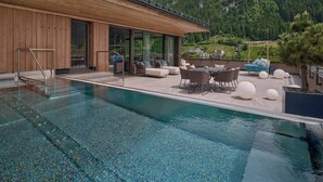 Un área de piscina moderna al aire libre con terraza de madera, asientos y vistas a un paisaje montañoso.
