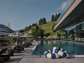 A poolside area with lounge chairs, umbrellas, and a clear view of a hillside. - DAS EDELWEISS - Salzburg Mountain Resort (Grossarl)