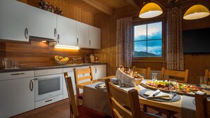 Une cuisine rustique dans une cabane en bois, avec des meubles blancs, une table à manger dressée et une fenêtre donnant sur les montagnes.