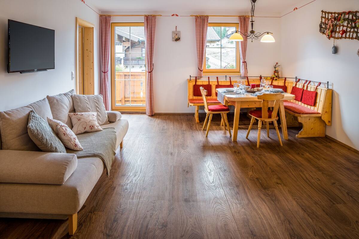 Una sala acogedora con un sofá, una mesa de comedor para cuatro personas y un banco.