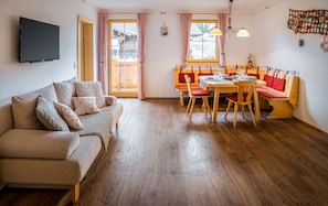 A cozy living room with a sofa, a dining table set for four, and a bench.