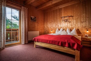 Una habitación con piso de madera, una cama, una ventana con cortinas, un radiador y una lámpara fijada a la pared.
