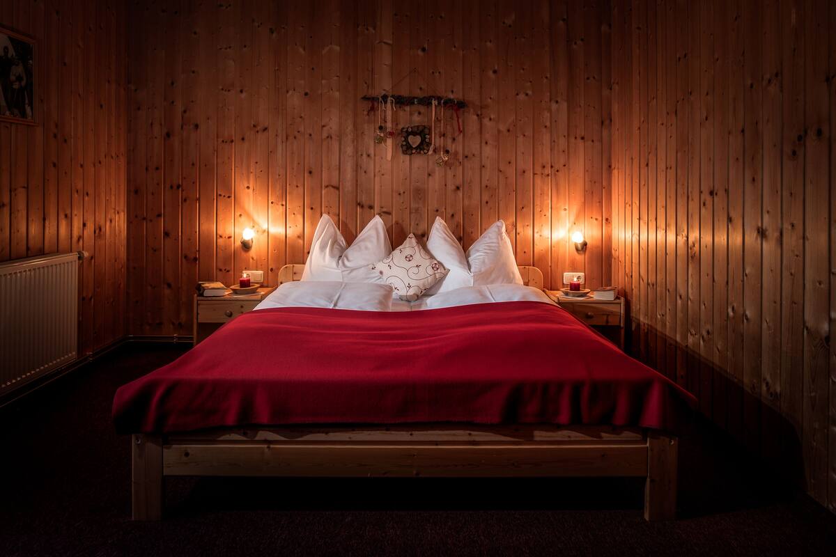 Una habitación con paneles de madera, una cama, dos mesitas de noche e iluminación en la pared.