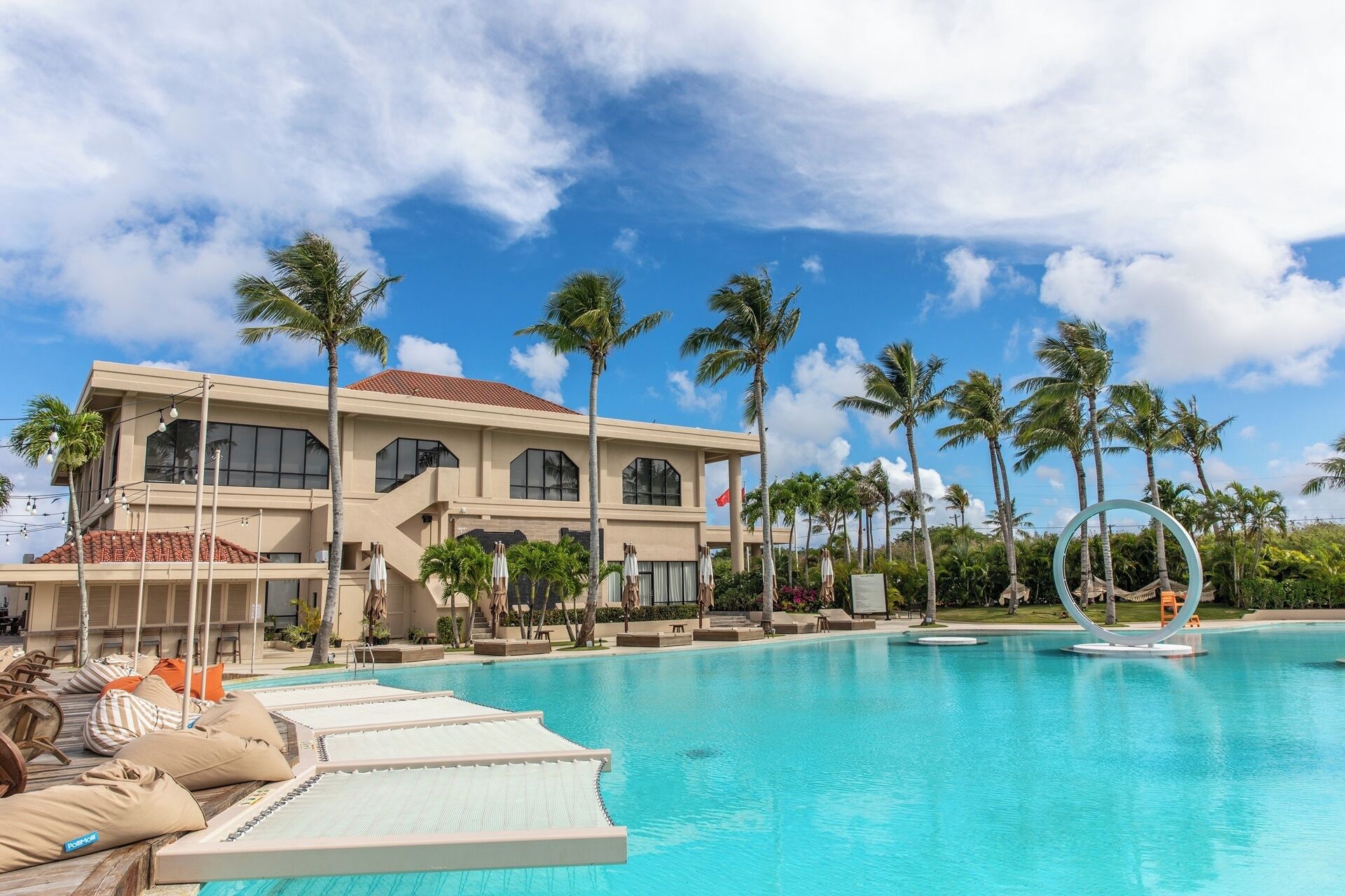 A resort with a swimming pool, palm trees, and a large building with multiple windows.