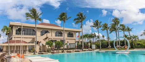 A resort with a swimming pool, palm trees, and a large building with multiple windows.