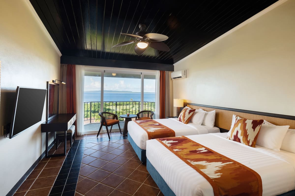 Habitación de hotel con dos camas, un escritorio, una silla y un balcón con vista al mar.