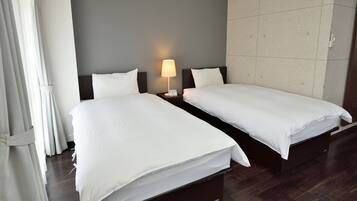 A hotel room with two single beds, a nightstand with a lamp, a curtain, and a tiled wall.