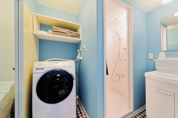A compact bathroom with a washing machine, a shower, and a sink.